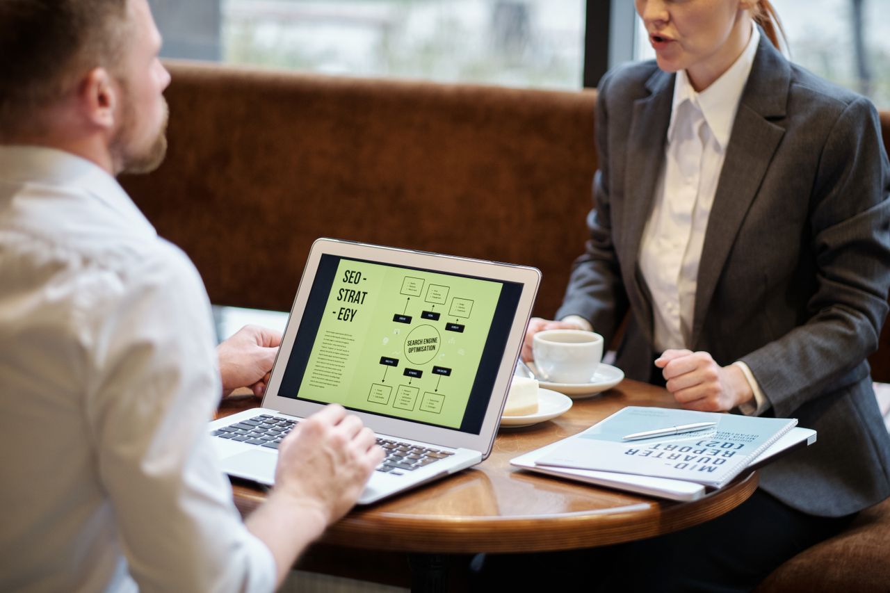 services-06 A man and woman engaged in a business meeting discussing SEO strategy in a cozy cafe setting.